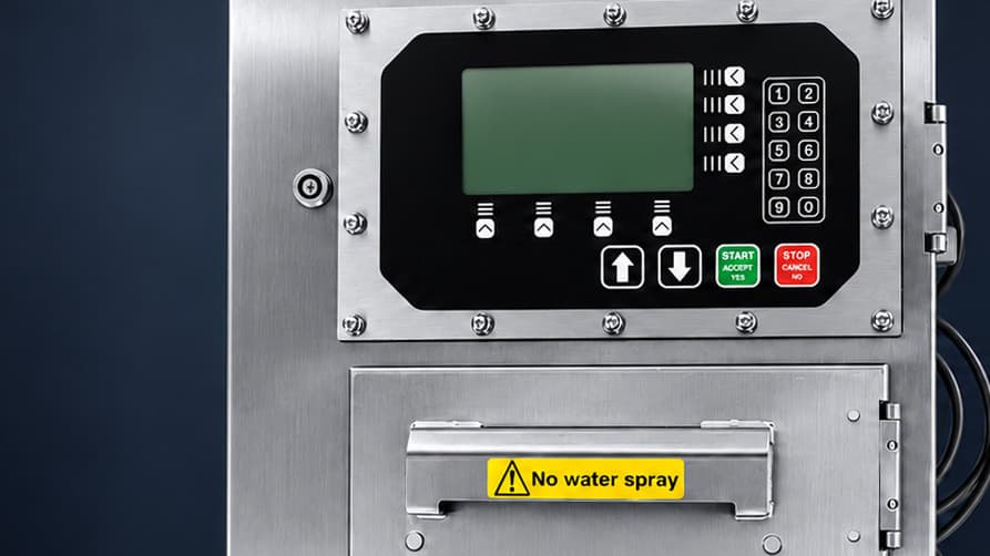 Stainless steel control enclosure with a sealed operator panel: a green display, soft-key buttons, a numeric keypad, arrow keys and green start and red stop buttons, above a hinged compartment with a handle and a yellow "No water spray" warning label